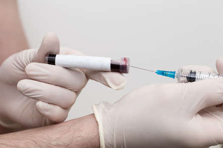 Hand with medical glove of scientist or doctor holds test tube with blood sample and blank label for own text and injectionの写真素材