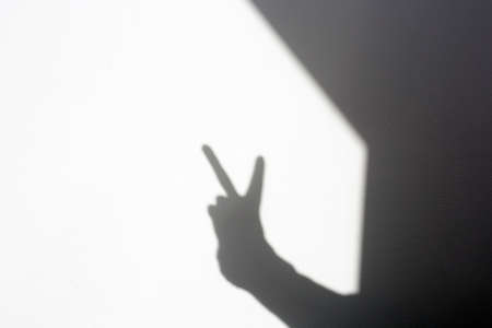 silhouette shadow hand doing peace sign on white wall, isolated homeの写真素材