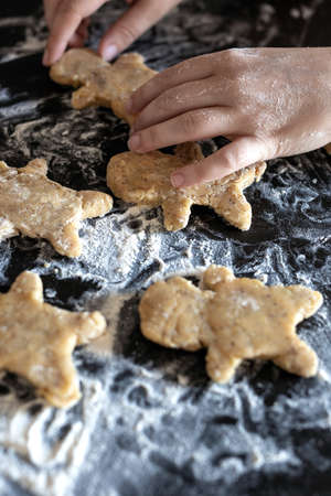 Person baking Gingerbread man cookies, Person hands in dough with flower in cozy kitchen close-up