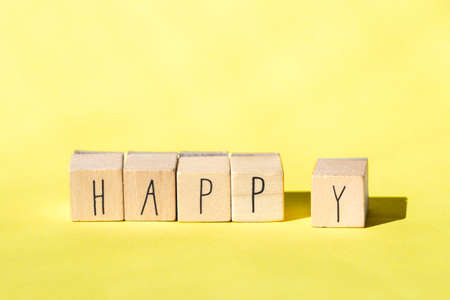 Wooden cubes with the word Happy on Bright Yellow background, Cheerful concept close-upの写真素材