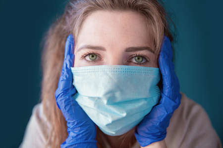 Young woman wearing protective gloves and face mask inside a home in quarantine looking bored and...