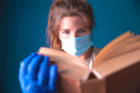 Young woman or student reading a book with protective mask and gloves for Corona Virus, Covid-19,...