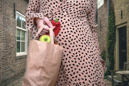 young woman holding a bag with fresh vegetables and fruit in the city street, apples and pepper