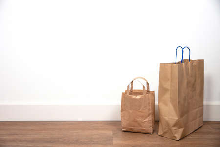 Close up of brown shopping bag against white wall on wooden floor, retro design space for textの写真素材