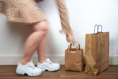 Young woman holding shopping bags, standing to a white wall, natural colors modern design. Retro concept cool movementの写真素材