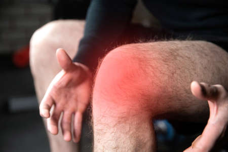 Portrait of a muscle fitness man reaching for his knee in pain, Men injury from exercise in the gym...