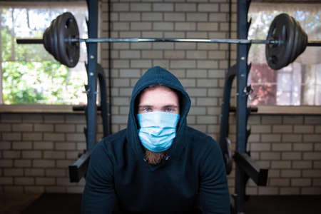 Young man in the gym with weights and protective mask and gloves for Coronavirus, Covid-19, fitness and corona conceptの写真素材