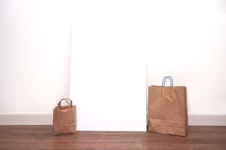 Brown blank shopping bags with blank poster frame against white wall, space for text. shopping concept close-upの写真素材