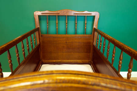 Antique retro wooden baby crib in babies room with green walls modern interior close-up