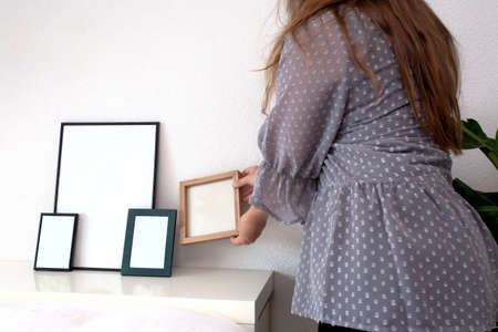 Woman holding empty photo or picture frame in a modern room near white wall, scandinavian design, retro interior space for textの写真素材