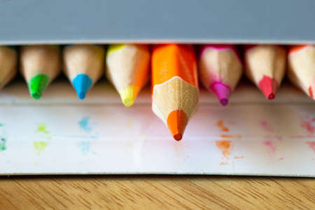 Colored pencils in a carton grey box, rainbow colors, orange pencil sticks out macro, school or office supplies backgroundの写真素材