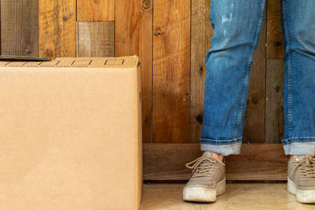 cardboard moving boxes in empty room with wooden wall background and copy space, moving in new flat or house concept, retro design with legs sneakers and jeans.の写真素材
