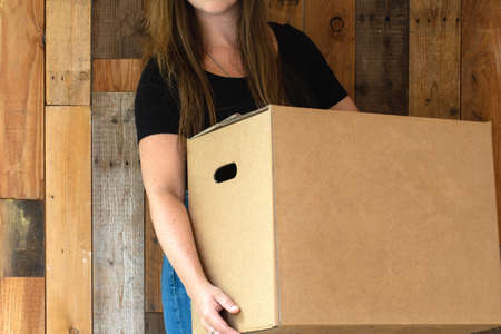 Happy young woman carrying a cardboard moving box for her new home, moving or new house conceptの写真素材