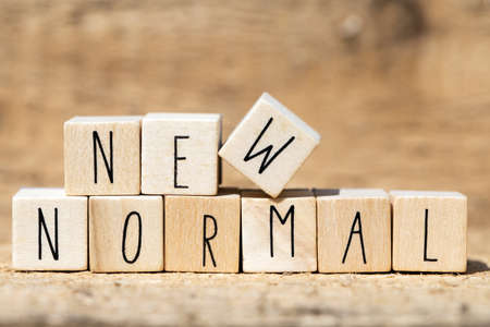 NEW NORMAL text on wooden cube. New normal life after covid-19 pandemic with social distancing and good hygiene on wooden backgroundの写真素材