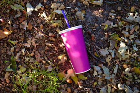 paper soft drink cup with plastic lid and straw thrown in the forest on the ground, milkshake or...