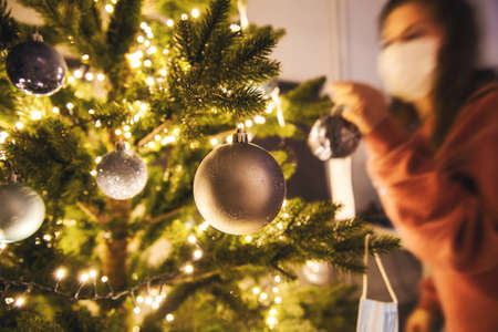 Young woman decorating a Christmas tree with medical safety mask for Covid-19, Coronavirus and Christmas concept, beautiful holidayの写真素材