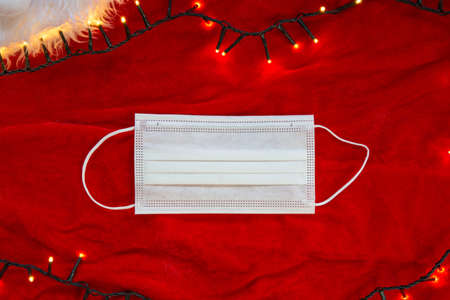 Two hands with protective gloves holding a medical face mask on red background with Christmas...