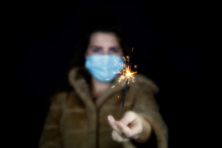 Happy new year, portrait of a young woman wearing medical mask and holding sparklers light in the...