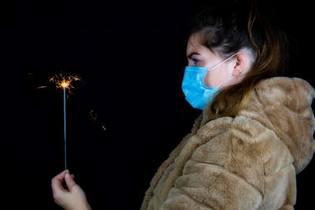 Happy new year, portrait of a young woman wearing medical mask and holding sparklers light in the...