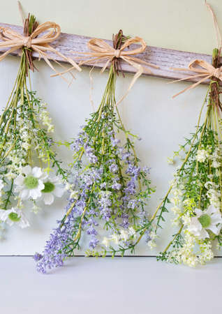 Various bright bouquet of dried flowers hanging on rope against wooden background, making dried...