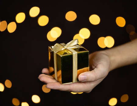 hand holding a gold gift box with gold ribbon,bokeh sparkle background, Christmas or Birthday...