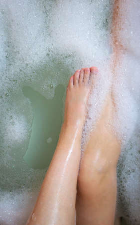 Womens legs in the bathtub, bathing with bubble bath foam top view, relaxtion beauty spa conceptの写真素材