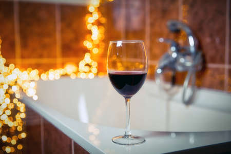 Close up of wine glass with red wine near bathtub with lights on the background, relaxtion and spa conceptの写真素材