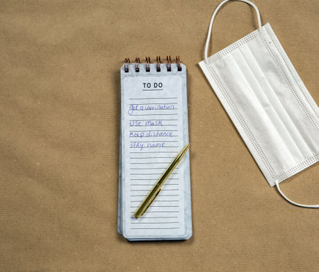 White medical masks and Notepad with measures against Coronavirus on brown paper background, COVID-19 concept modern design top view, copy spaceの写真素材