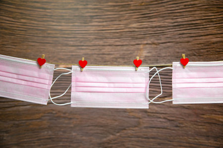 Pink protective medical mask hanging with clothes pegs in heart shape isolated on white background,...