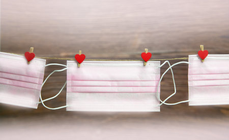 Pink protective medical mask hanging with clothes pegs in heart shape isolated on white background,...