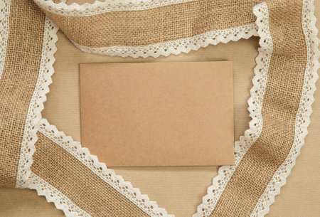 Flat Lay composition with blank brown plain greeting card surrounded with natural burlap ribbon on craft paper background texture, top view design, copy space natural colorsの写真素材
