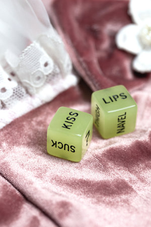 Two dice for erotic sexual game with the text kiss lips and neck on pink satin fabric background,...
