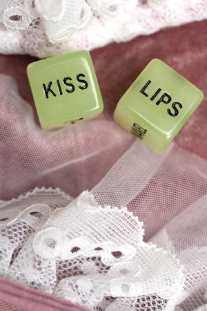 Two dice for erotic sexual game with the text kiss lips and neck on pink satin fabric background,...