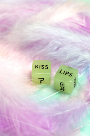 Two dice for erotic sexual game with the text Kiss lips for Valentines Day sex, romantic, sensual concept with pastel colored feather background sensual couple relation toyの写真素材
