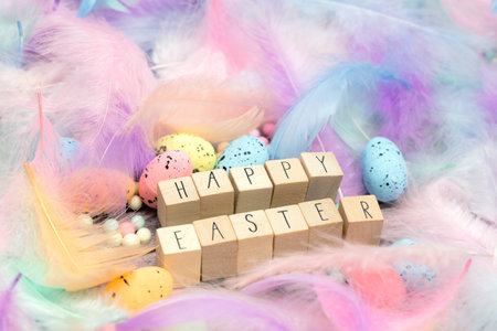 Happy Easter written with wooden cubes surrounded with beautiful pastel colored decorative feathers...