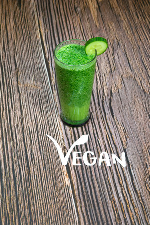 Healthy fresh green shake or smoothie with green vegetables spinach, avocado, apple on wooden background texture with the text Vegan top view, copy spaceの写真素材