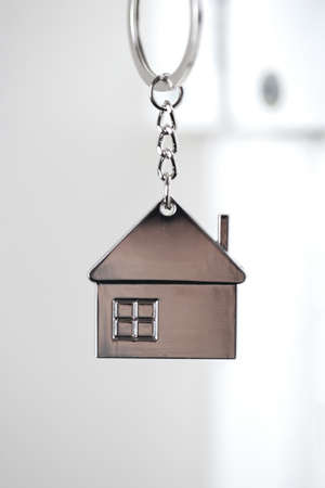 Silver house key in white door, with little keychain house, opening door to new house, home, investment, real estate concept, space for textの写真素材