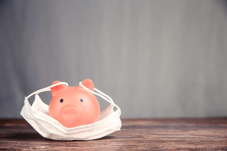 Inserting coin in piggy bank for savings with protective medical mask for pandemicの写真素材