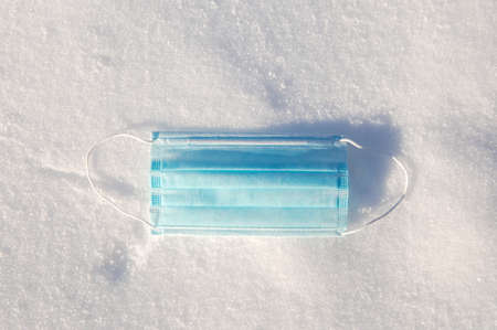 Protective blue medical mask for virus lies in the snow, Covid-19, pandemic,winter,virus,health concept, copy space backgroundの写真素材