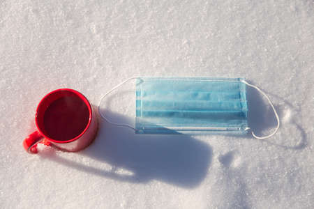 Red mug with hot coffee,tea or chocolate milk and protective blue medical mask for coronavirus...