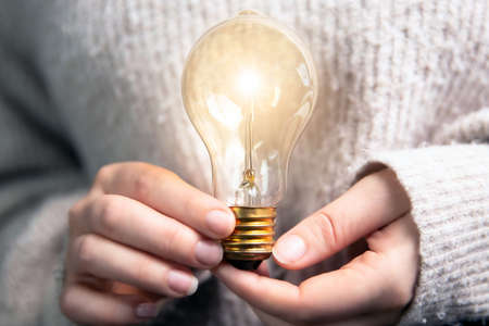 Female hand holding a shining light bulb, Great idea, innovation and inspiration, business concept backgroundの写真素材
