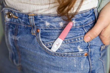 Young woman with positive pregnancy test in pocket of jeans close-up motherhood happiness modern retro backgroundの写真素材