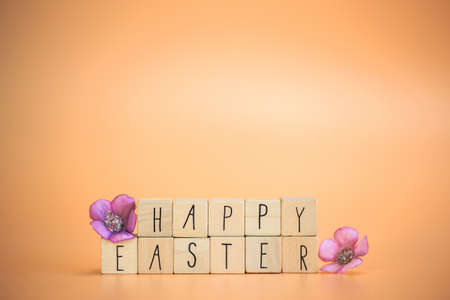Happy Easter Holiday text on bright orange pastel colored background with purple spring flowers, concept for greeting card,spring,Easter with copy spaceの写真素材