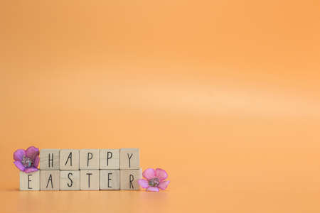 Happy Easter Holiday text on bright orange pastel colored background with purple spring flowers, concept for greeting card,spring,Easter with copy spaceの写真素材