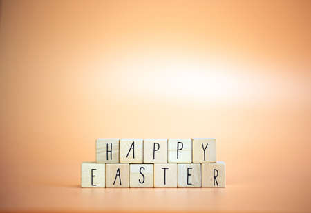Happy Easter written with pastel colored orange background and bright spring flowers, greeting...