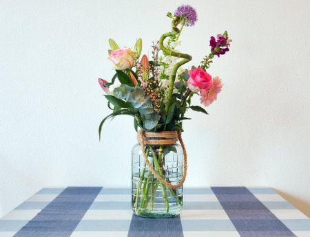 Beautiful fresh bright and colorful spring flowers in a glass vase, bright bouquet with the colors pink and purple on table in modern home near white wall. Retro summer decorationの写真素材