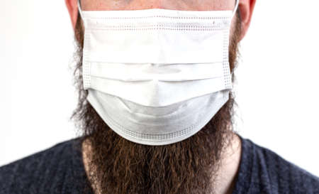 Caucasian young bearded adult man wearing a protective or surgical mask to avoid pollution and contagious virus and diseases isolated on white backgroundの写真素材