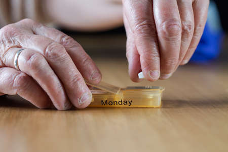 Closeup of an elderly senior womans hands taking her medication for the week in a pill box on wooden table, business,health conceptの写真素材