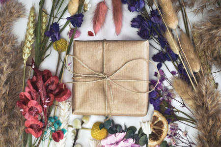 Gift box wrapped in eco friendly craft paper surrounded with colorful fresh dried flowers top view,...