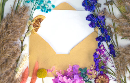 Blank white paper with craft paper envelope and colorful dried spring flowers and reed , blossom,...